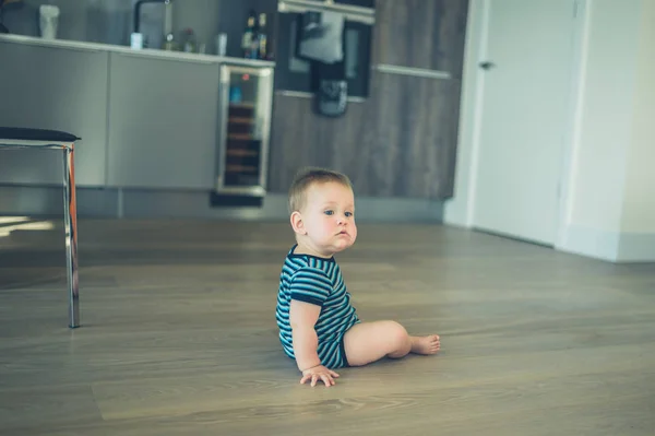 Malé dítě sedí na podlaze v kuchyni — Stock fotografie