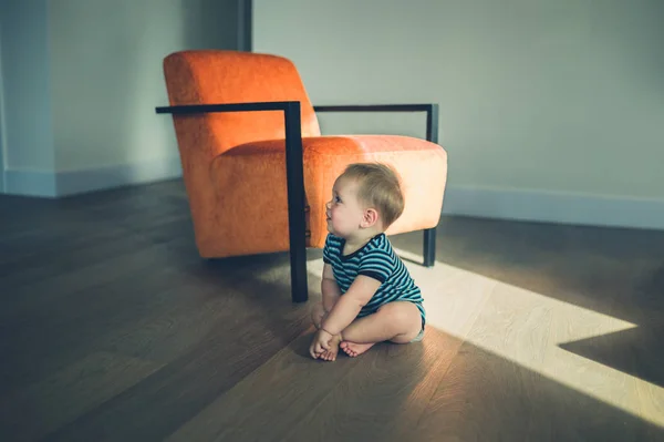 Cute little baby sitting by a chair in the sunlight — Stock Photo, Image