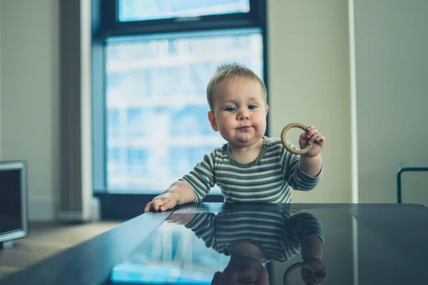 Маленька дитина з кільцем зубів стоїть за столом — стокове фото
