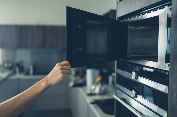 Mujer joven abriendo el microondas — Foto de Stock