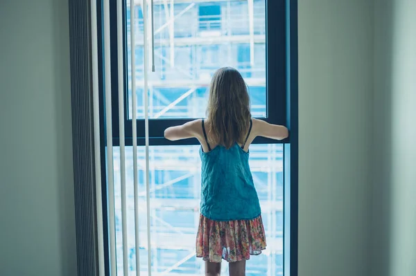 Mladá žena při pohledu z okna bytu — Stock fotografie