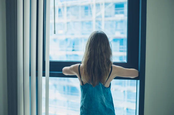 Jovem mulher olhando para a janela do apartamento — Fotografia de Stock