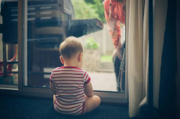 Baby sitting by window with man outside — Stock Photo, Image