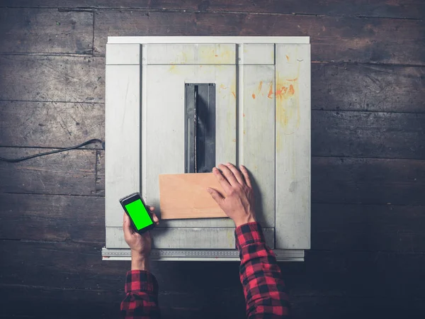 Homem com chave chroma telefone inteligente e tablesaw — Fotografia de Stock