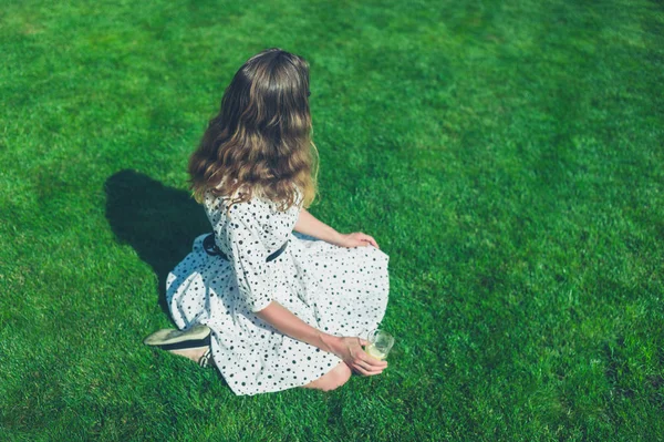 Žena v šatech sedí na trávníku v létě — Stock fotografie