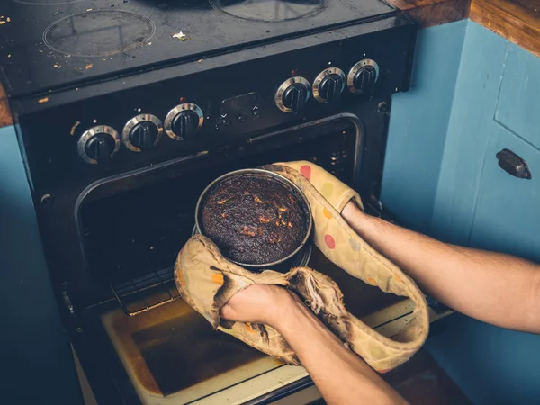 Мужчина вытаскивает сгоревший торт из духовки — стоковое фото