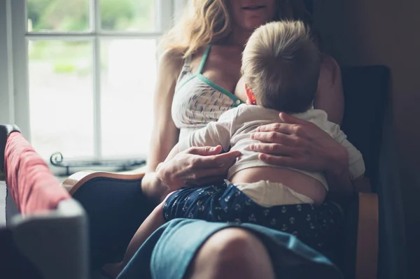 Mother breastfeeding baby by the window at home — Stock Photo, Image