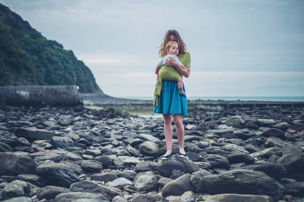 Moeder met baby in draagdoek op het strand in het najaar — Stockfoto