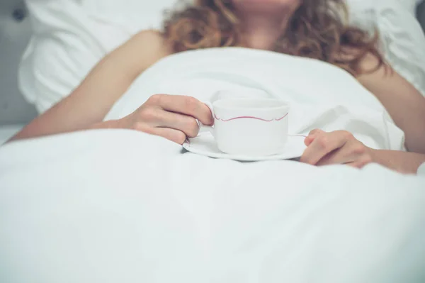 Mladá žena pít čaj v posteli — Stock fotografie