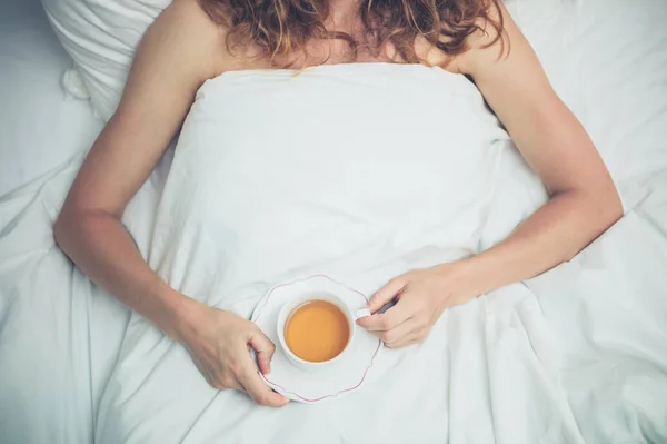 Mujer joven bebiendo té en la cama — Foto de Stock