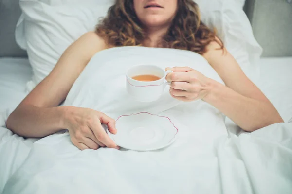 若い女性がベッドの中でお茶を飲む — ストック写真