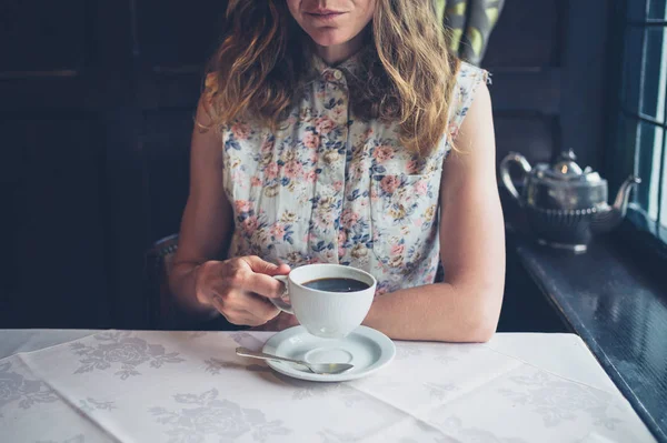 Vrouw aan tafel bij raam koffie drinken — Stockfoto