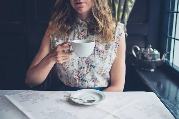 Vrouw aan tafel bij raam koffie drinken — Stockfoto