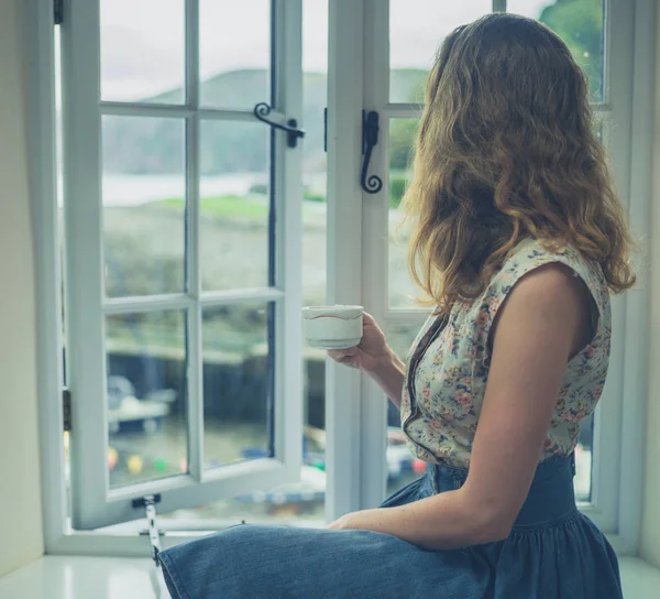 Mujer joven bebiendo té junto a la ventana — Foto de Stock
