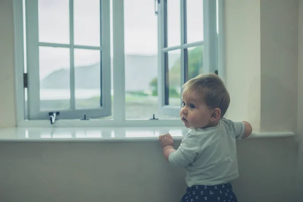 Kleines Baby steht am Fenster eines Landhauses — Stockfoto