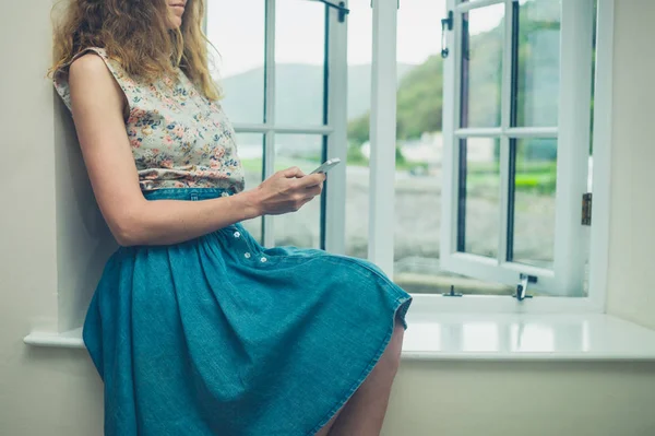 Vrouw met behulp van haar telefoon door raam van het landhuis — Stockfoto