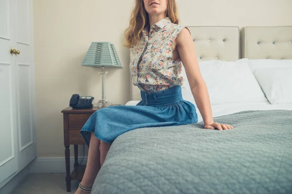 Young woman sitting on bed in hotel room — Stock Photo, Image