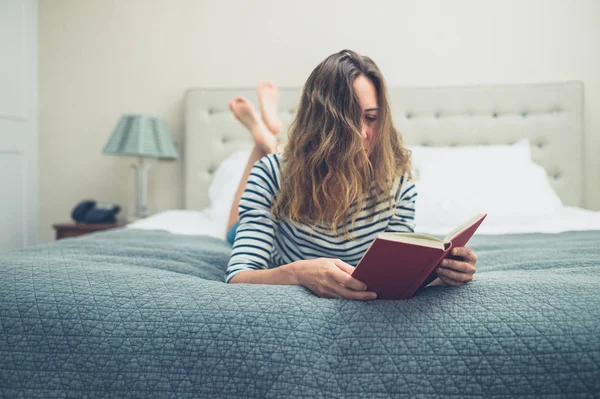 Young woman reading book on bed — Stock Photo, Image