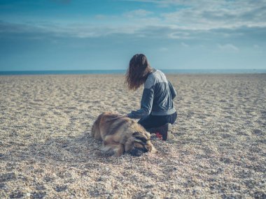Büyük köpek ile sahilde oturan genç kadın