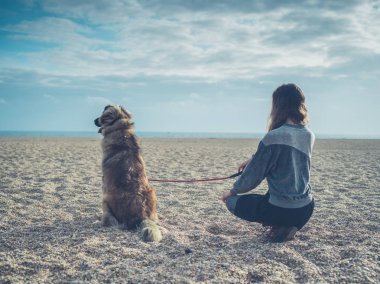 Büyük köpek ile sahilde oturan genç kadın