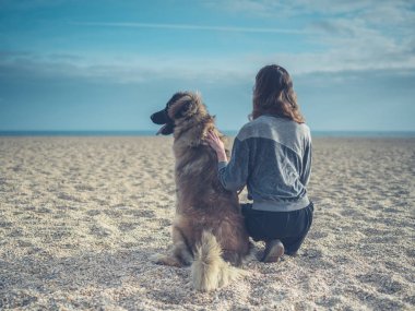Büyük köpek ile sahilde oturan genç kadın
