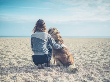 Büyük köpek ile sahilde oturan genç kadın