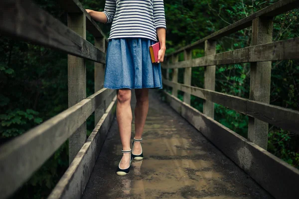 Vrouw met boek op brug in bos — Stockfoto