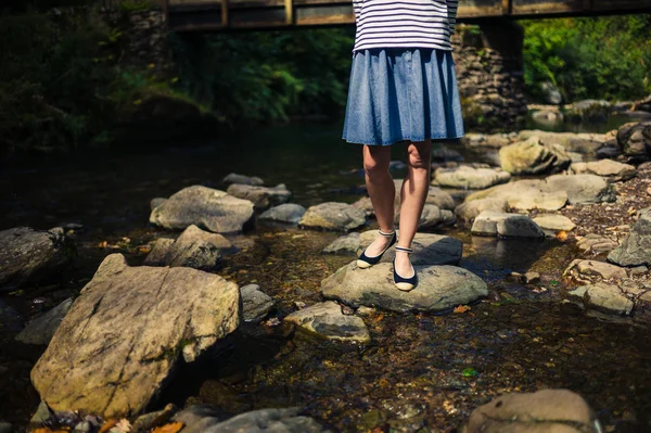 Donna in gonna in piedi su rocce nel fiume — Foto Stock