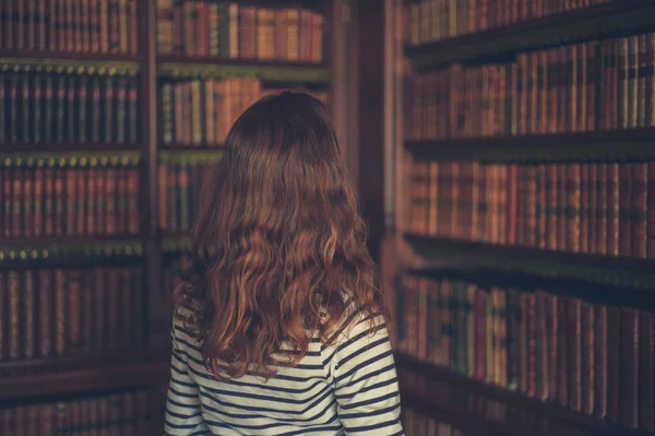 Mulher olhando para livros em uma biblioteca antiga — Fotografia de Stock