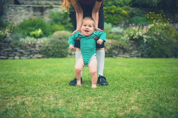 Mother helping baby walk on lawn — Stock Photo, Image