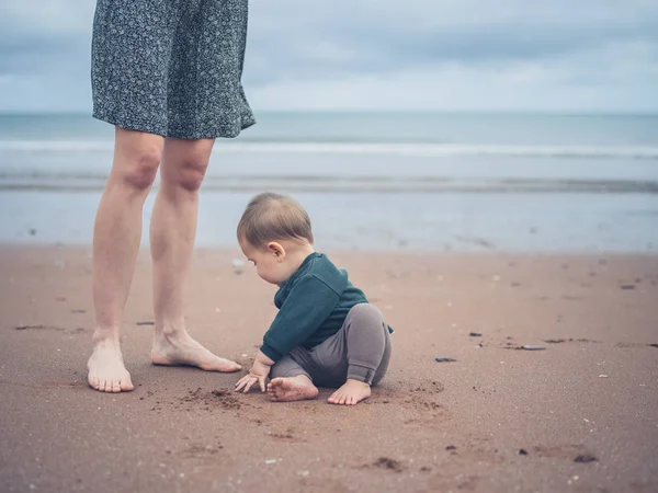 Pequeño bebé jugando por piernas de madre en la playa — Foto de Stock