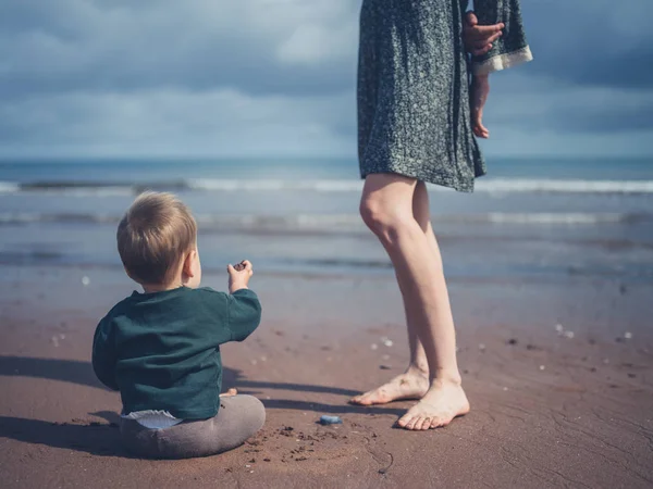 Pequeño bebé jugando por piernas de madre en la playa — Foto de Stock
