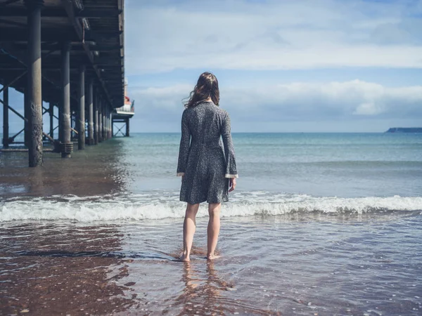 Mujer joven parada junto a un muelle en la playa — Foto de Stock