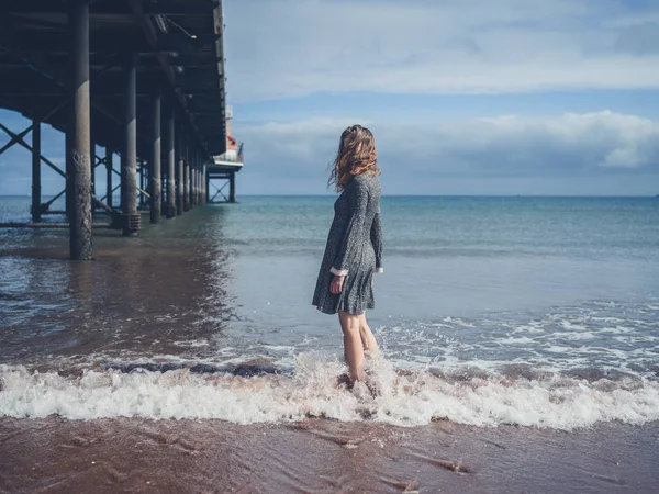 Mujer joven parada junto a un muelle en la playa —  Fotos de Stock