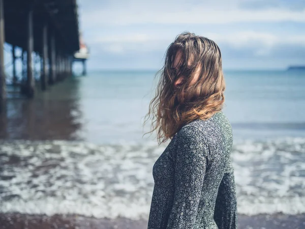 Jonge vrouw door een pier op het strand — Stockfoto