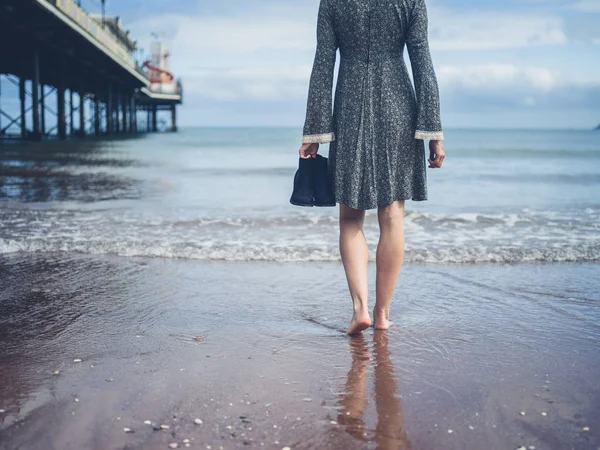 Woman walking on beach with shoes in hand — Stock Photo, Image