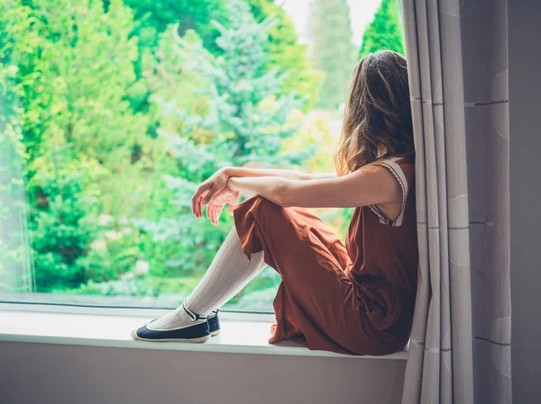 Молода жінка сидить біля вікна — стокове фото