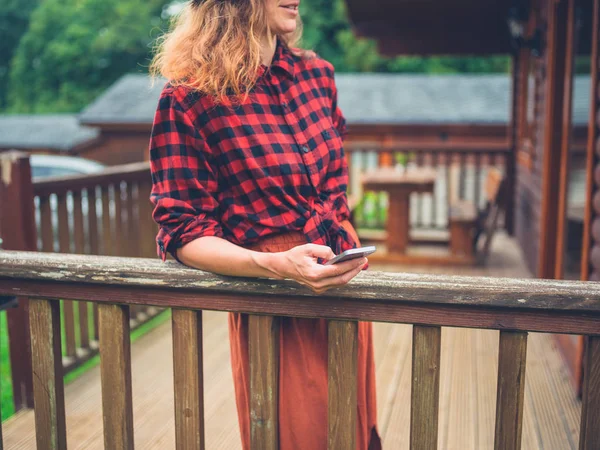 Young woman with phone on porch of cabin — Stock Photo, Image