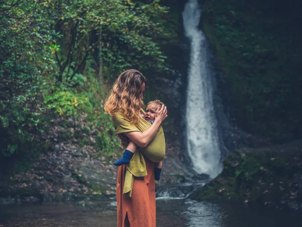 Mother with baby standing by waterfall — Stock Photo, Image