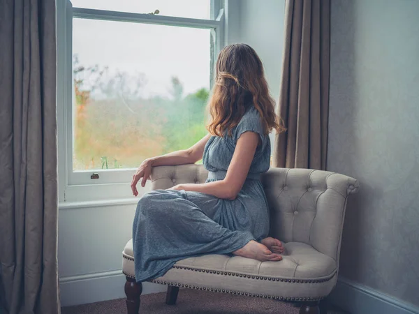 Jonge vrouw dagdromen door raam — Stockfoto