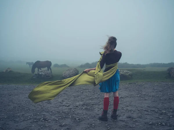 Donna con sciarpa nel vento guardando i cavalli selvatici — Foto Stock