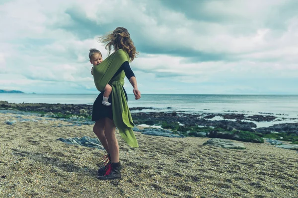 Mother with baby in sling spinning on beach — Stock Photo, Image