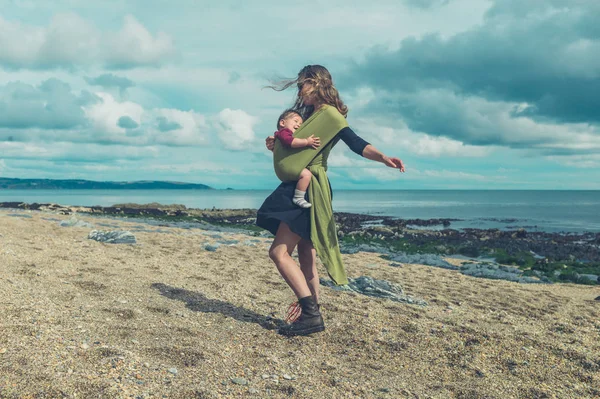 Matka z dzieckiem w chuście przędzenia na plaży — Zdjęcie stockowe