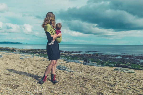 Мать с ребенком в стропе стоит на пляже — стоковое фото