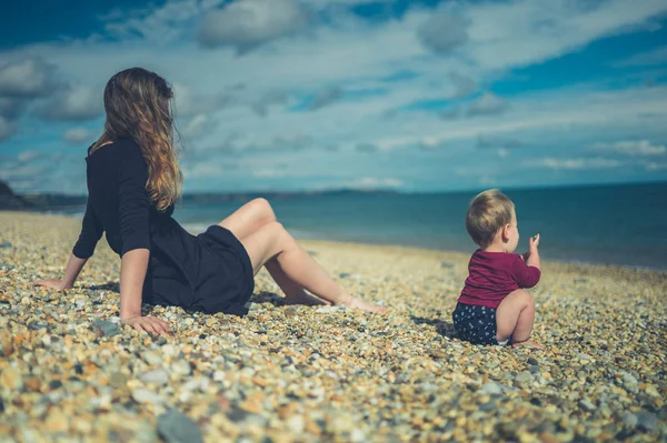 Joven madre sentada en la playa con su bebé — Foto de Stock