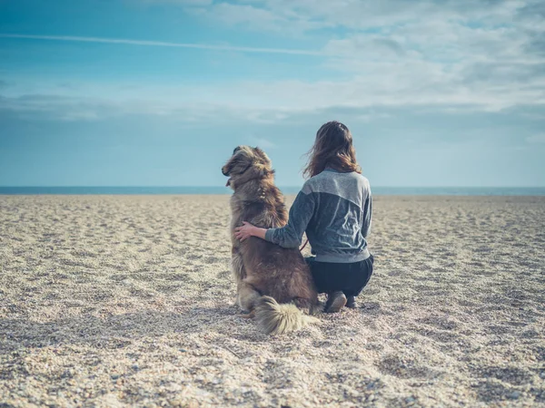 Mujer joven sentada en la playa con un perro grande — Foto de Stock