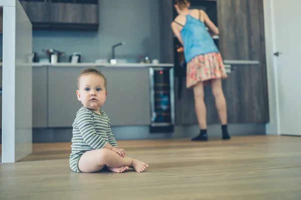 Pieni vauva keittiön lattialla äidin kanssa taustalla — kuvapankkivalokuva