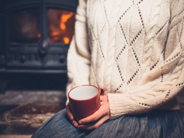 Genç bir kadın olarak beyaz bir jumper bir kupa içme şömine başına oturmuş