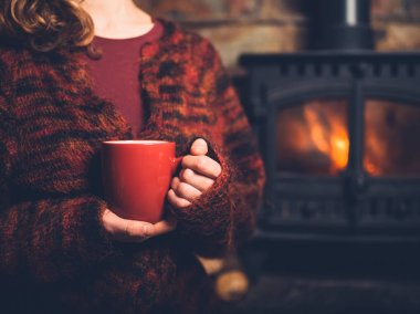 Genç bir kadın olarak kırmızı bir jumper bir kupa içme şömine başına oturmuş