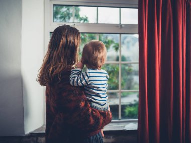 Genç bir wmother küçük yürümeye başlayan çocuk oğlu ile pencereden dışarı bakıyor